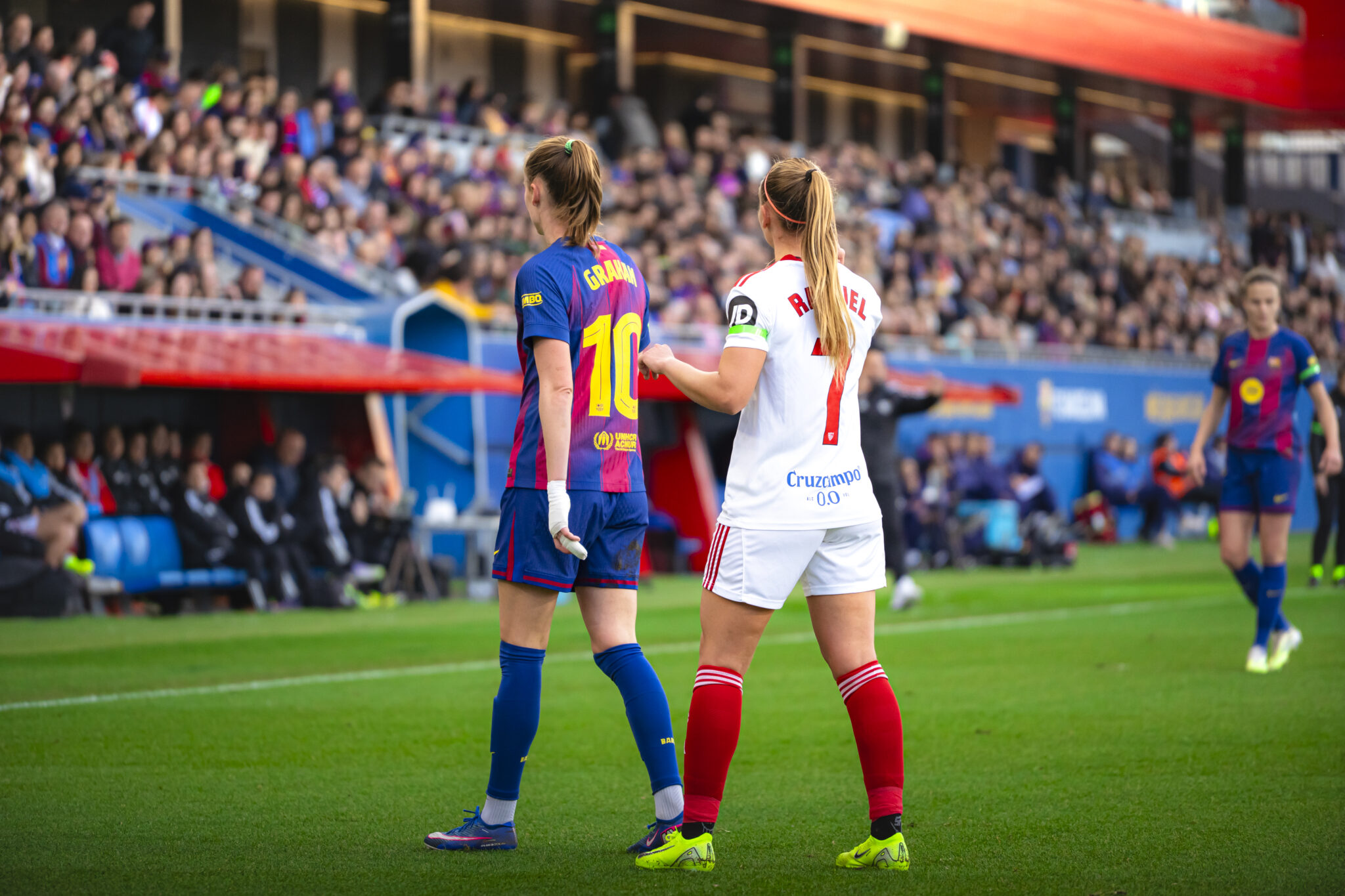 Graham Hansen jugadora del FC Barcelona Femenino de espaldas observa el desarrollo del partido desde el terreno de juego junto a una jugadora del Sevilla FC Femenino.